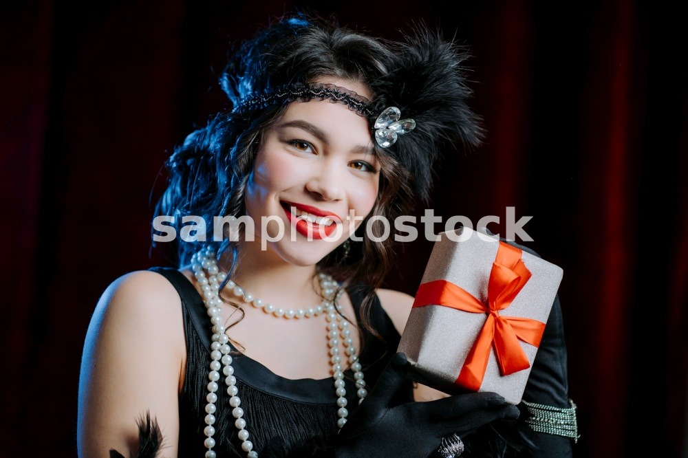 Joyful vintage styled woman dressed in Art Deco era holding gift box with bow on velours background. She is glad to get present. retro, party, fashion concept. High quality photo. Joyful vintage styled woman dressed in Art Deco era holding gift box with bow on velours background. She is glad to get present. retro, party, fashion concept.